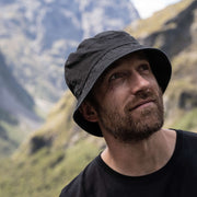 Model wearing Washed Black Out There Organic Bucket Hat in Fiordland, NZ.