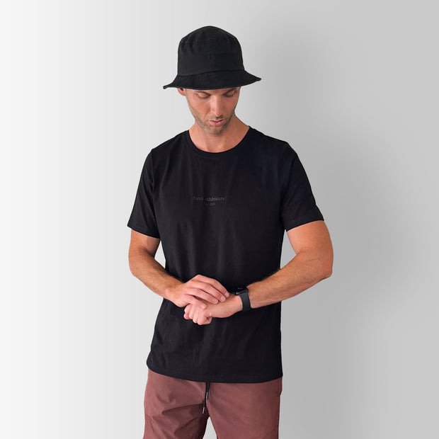 Front view of model wearing a black Out There Organic Logo Tee in studio.